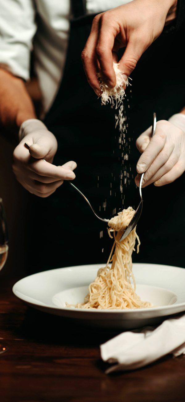 Close-up of the chef's hand pouring grated cheese onto the pasta